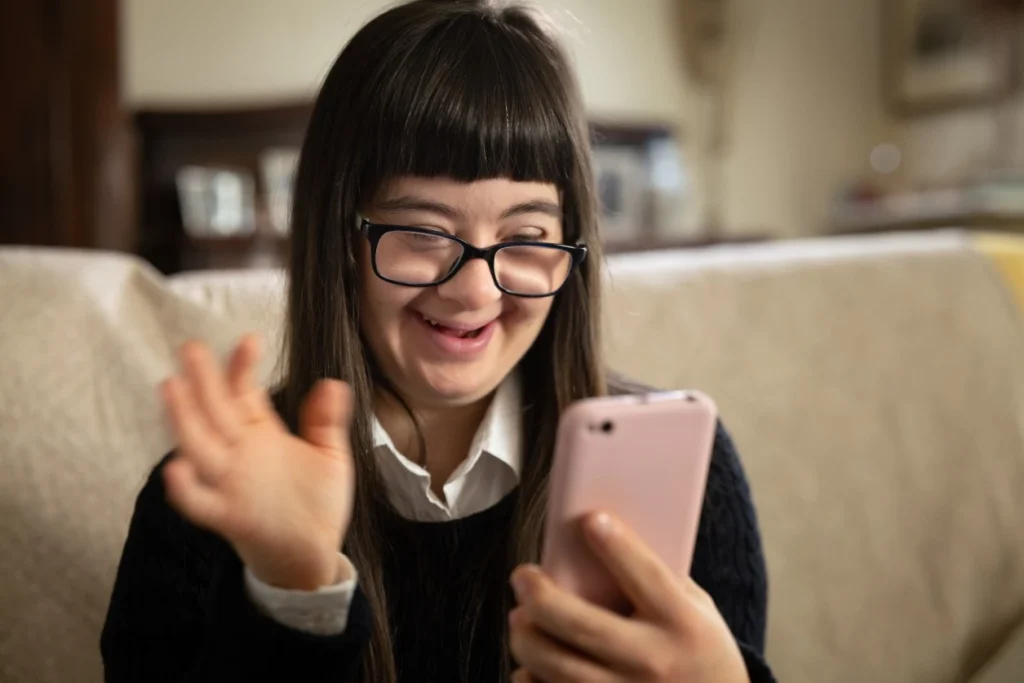 Girl with down syndrome looking at phone and waving on FaceTime call