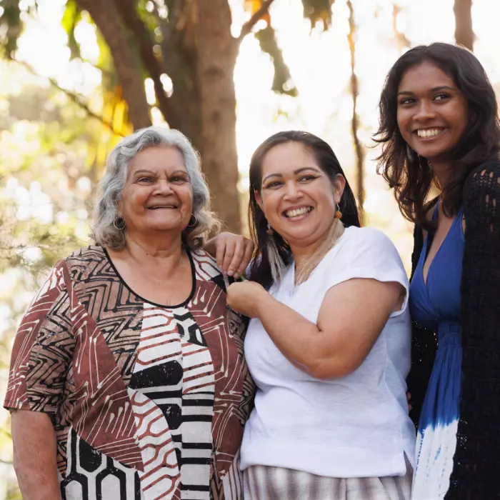 Three indigenous women standing together and smiling, looking away from the camera