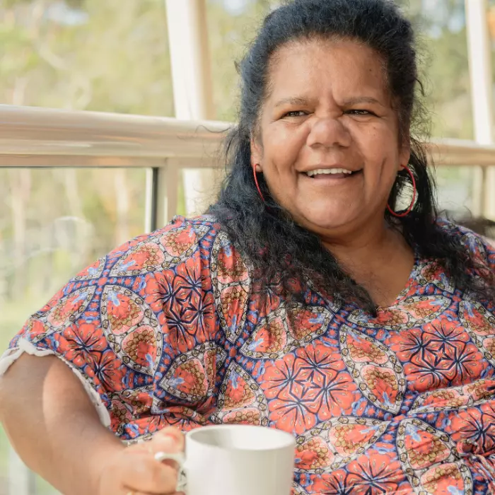 Indigenous woman sitting outside with a mug smiling