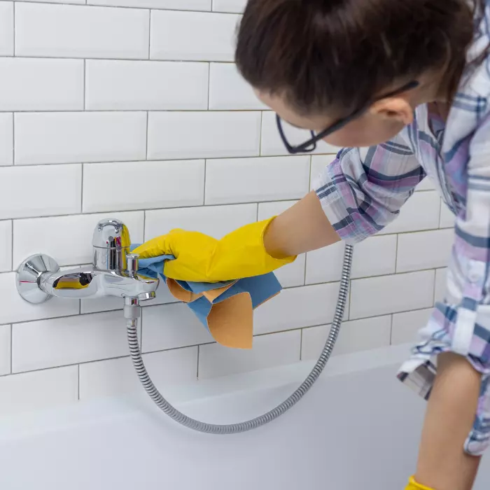 Woman cleaning bath tap in bathroom