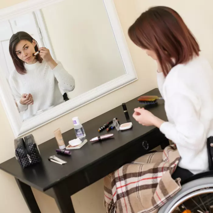 Disabled woman in wheelchair doing makeup in mirror